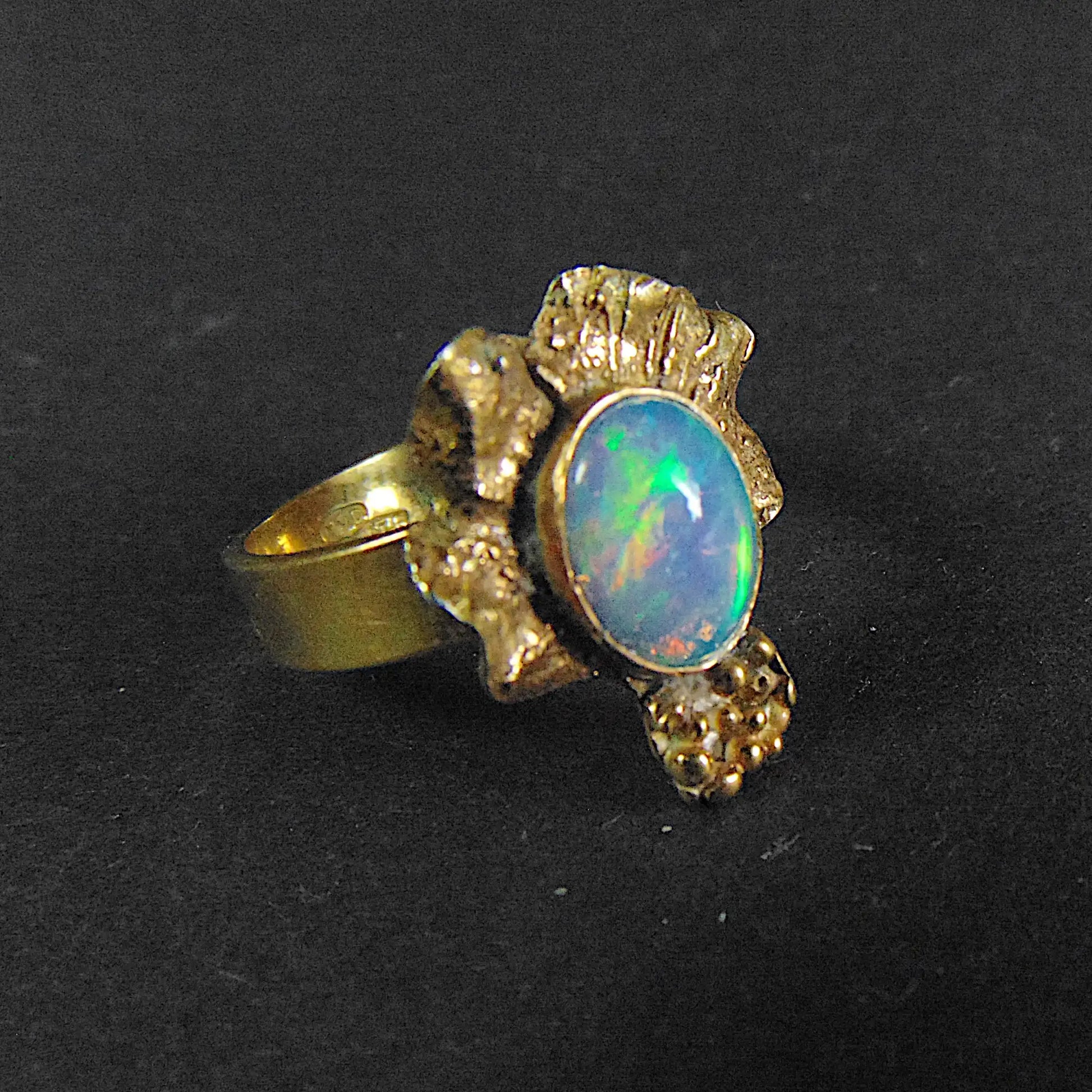 Elegancki pierścionek EPIR: opal etiopski (ok. 10x8 mm) otulony złoconą, rzeźbioną oprawą ze srebra, na tle ekspozytora.